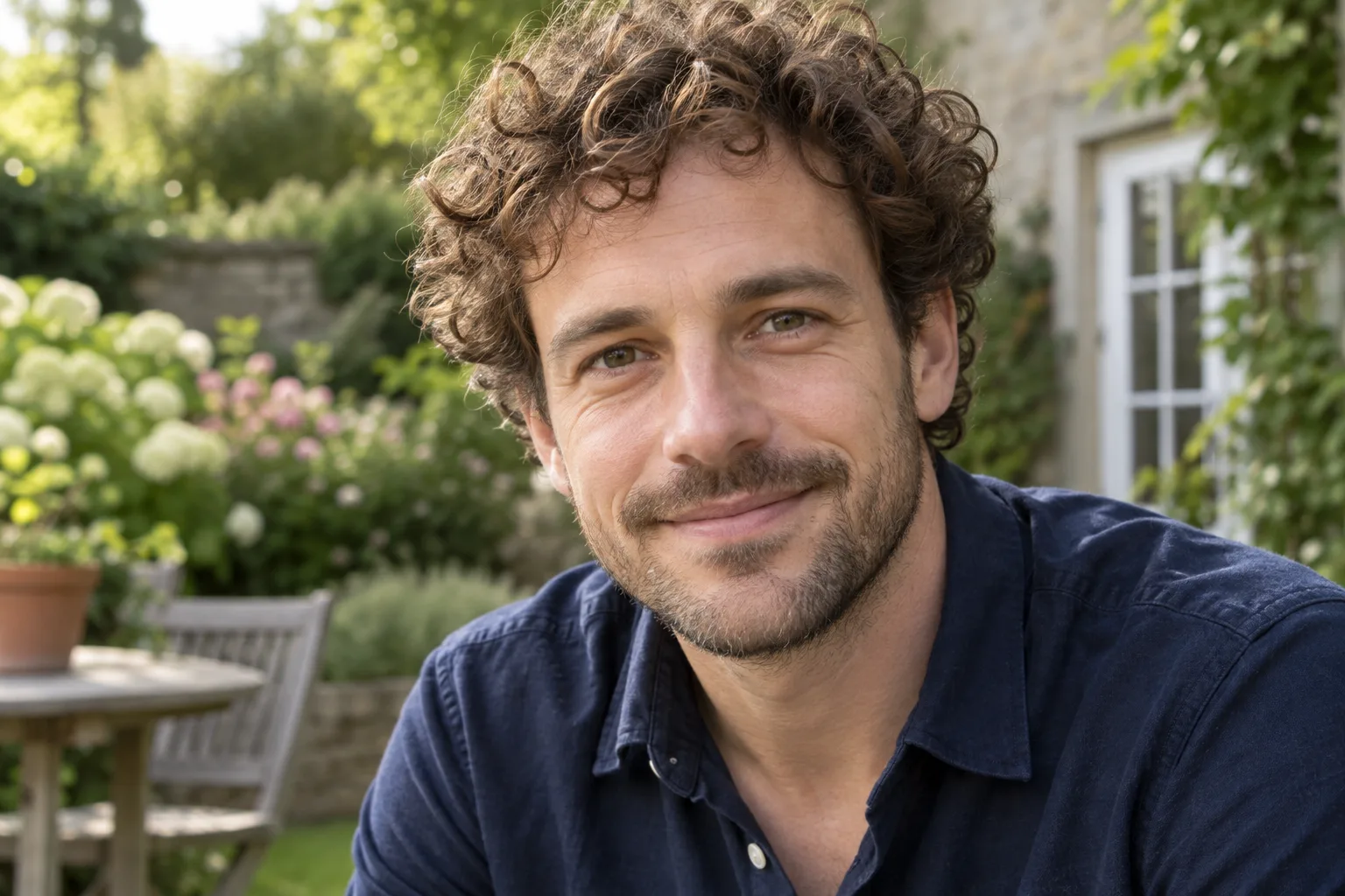 Sharp portrait of a curly-haired man against a garden background